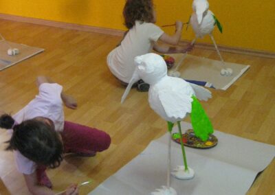 Zwei Kinder arbeiten an Pappmaché-Vögeln, die vor ihnen auf dem Boden stehen.